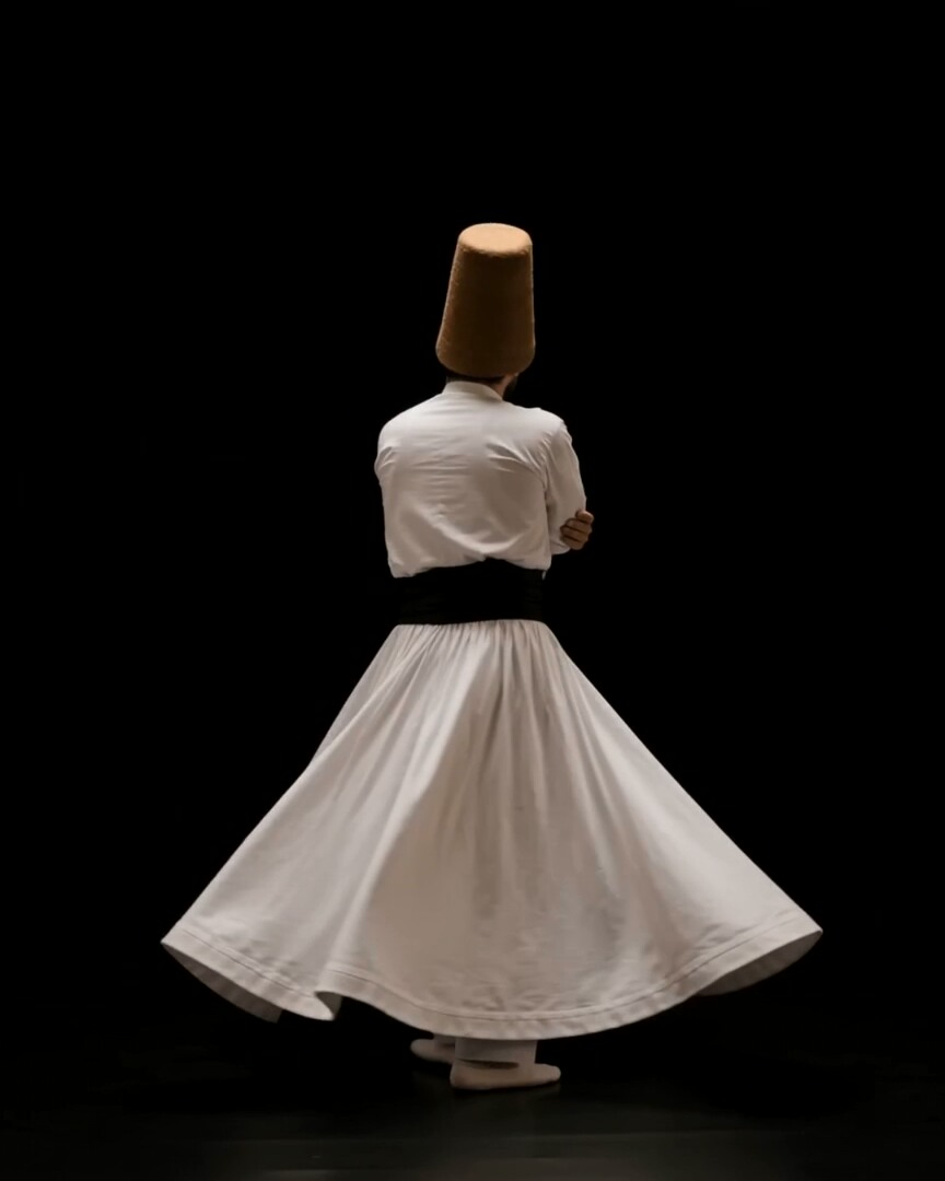 A figure in pale robes moving against a black background, film frame